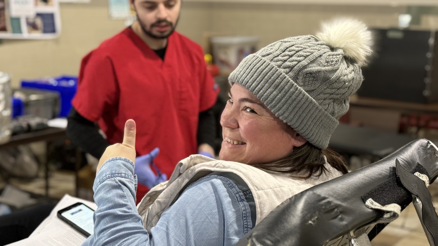 blood donor in winter hat smiling with thumbs-up