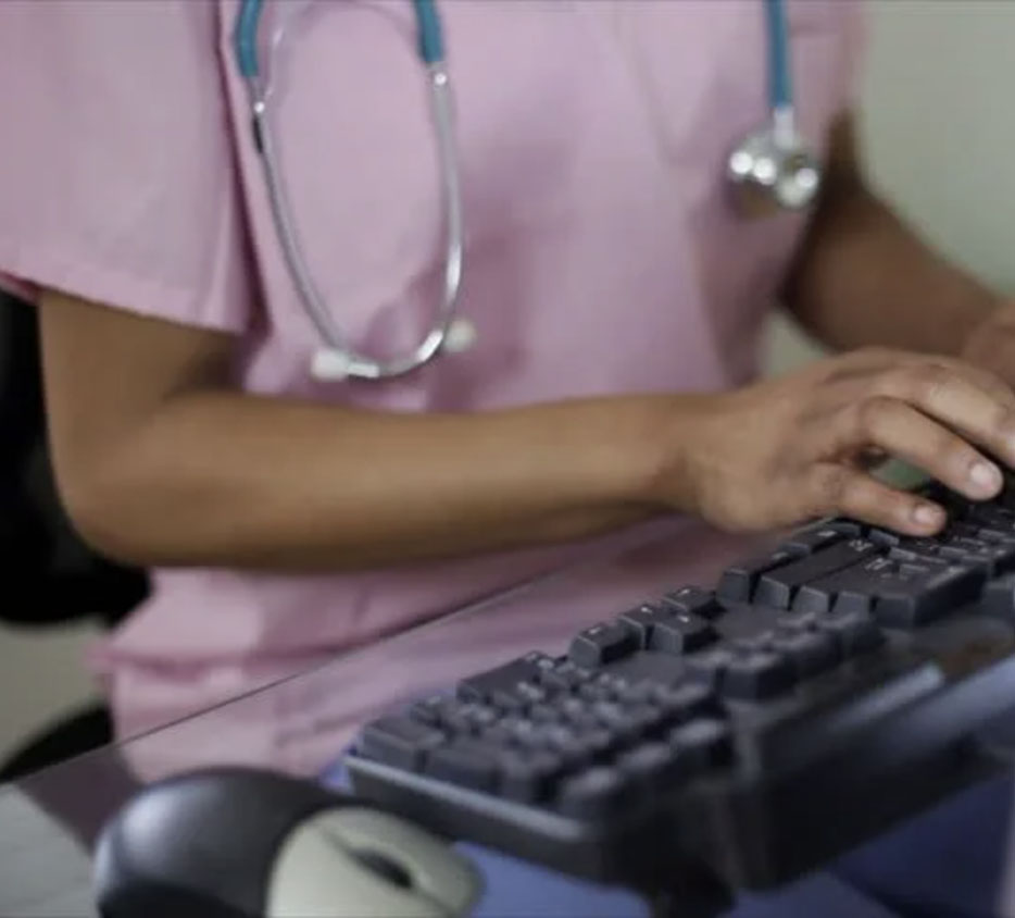 Medical personnel wearing a stethoscope, typing information into a computer