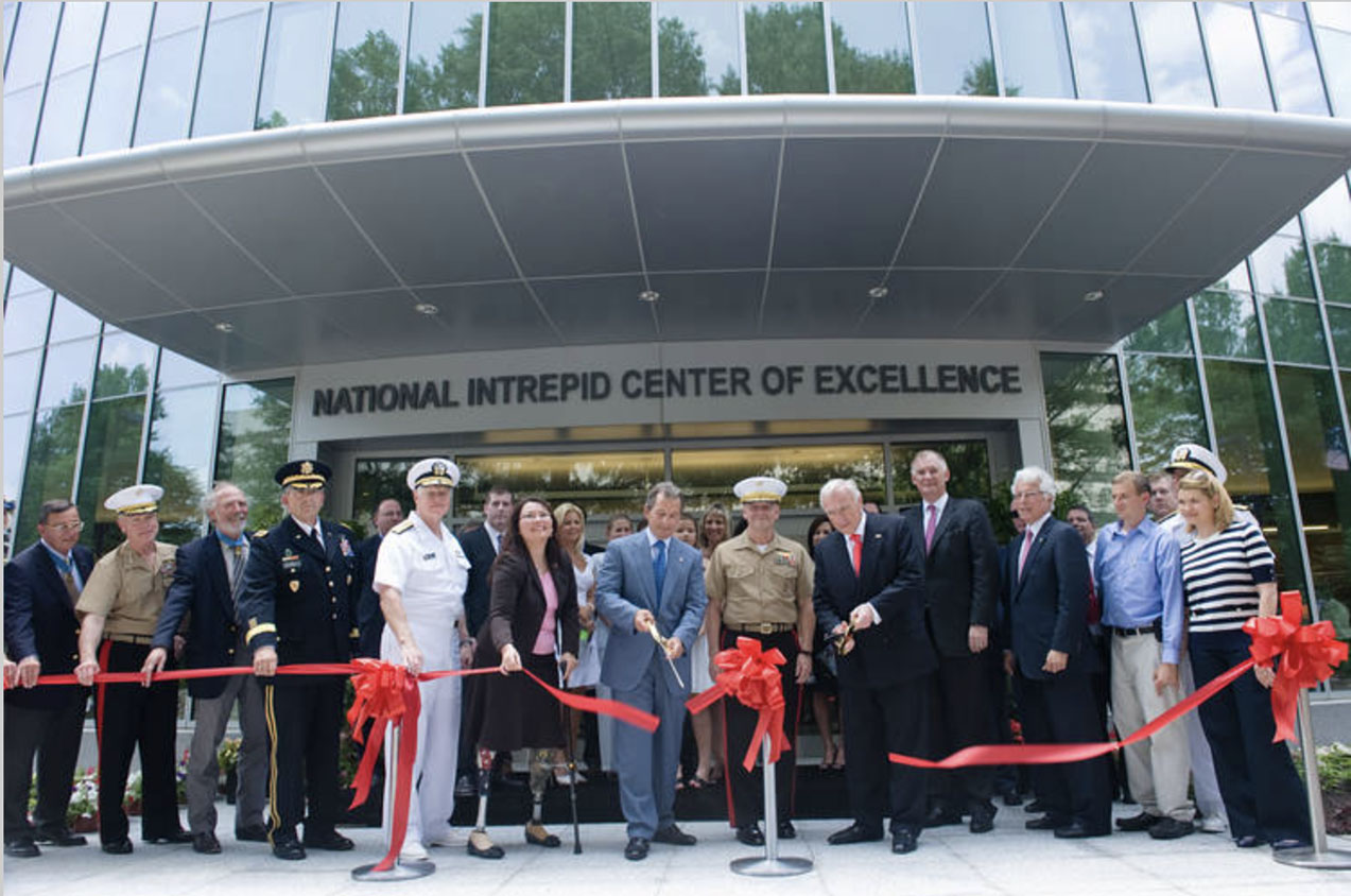 Military and civilian personnel cutting the red ribbon outside of a building for The National Intrepid Center of Excellence