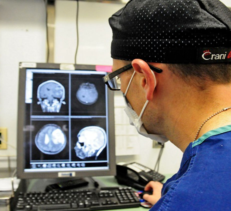 Medical personnel wearing a mask is looking at a screen with X-ray images of a person's skull