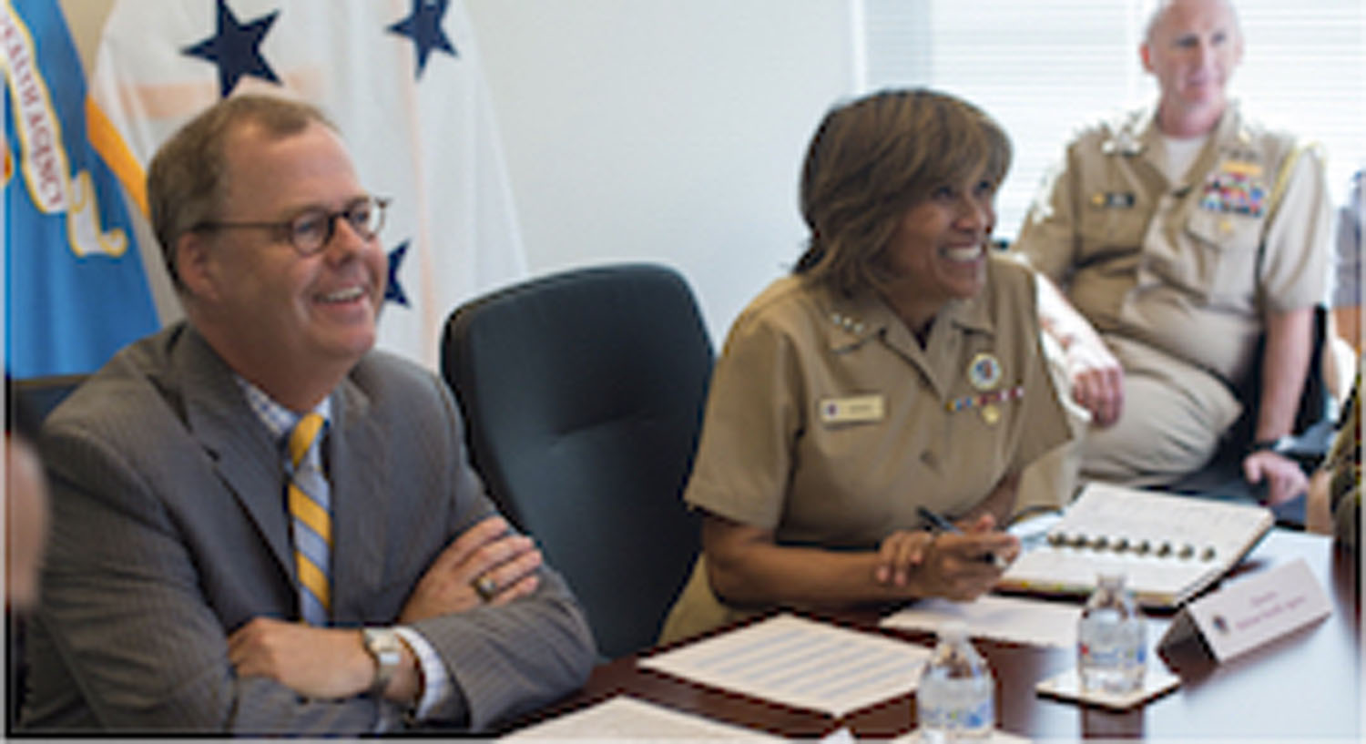 Admiral Bono and other DHA personnel sitting at a desk, smiling