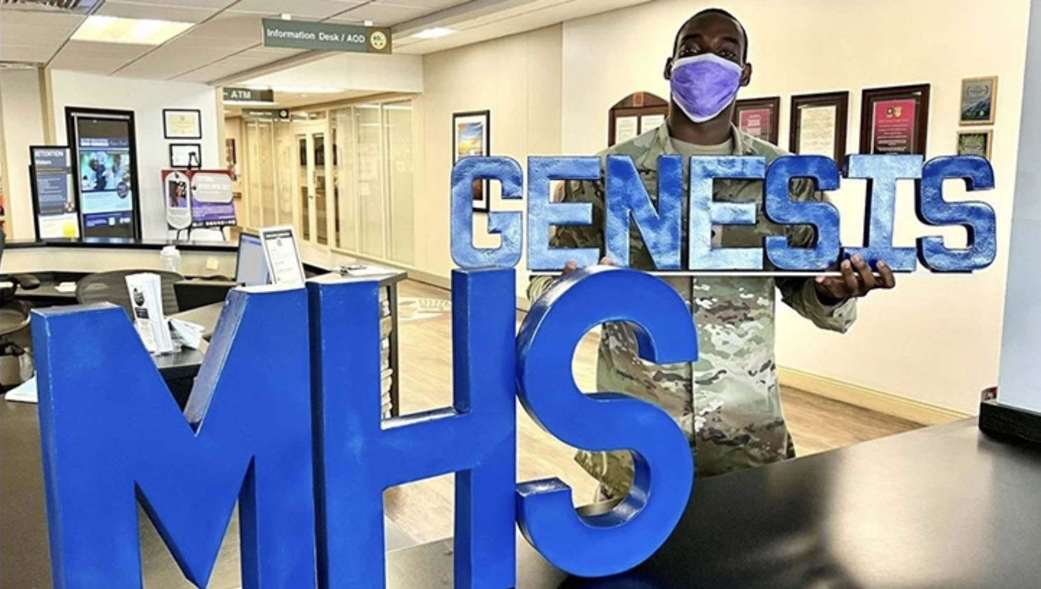 Soldier holding the word "GENESIS" next to the word "MHS" on a table