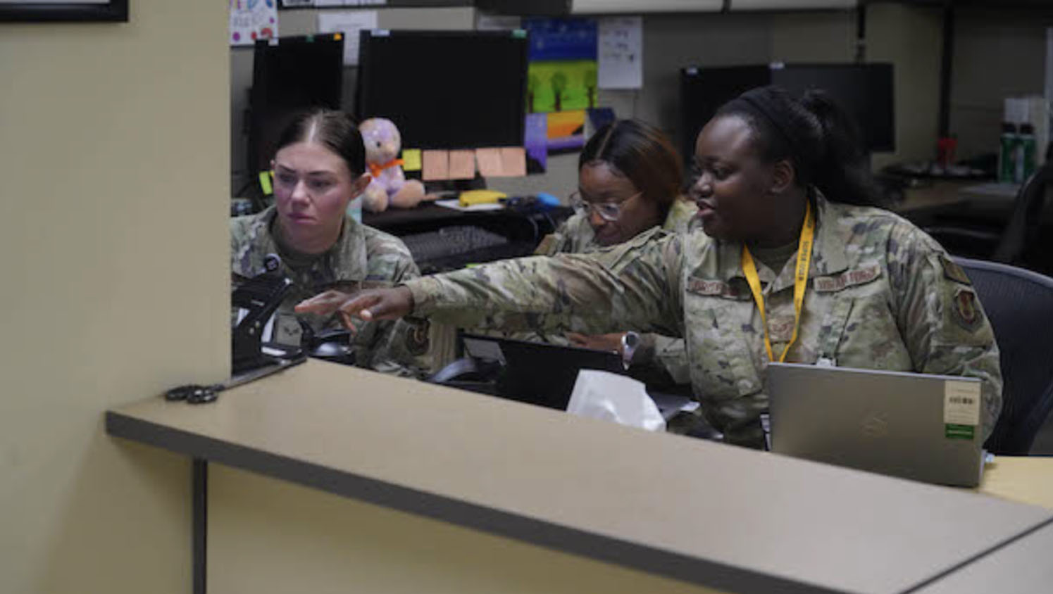Three military personnel with laptops in an office
