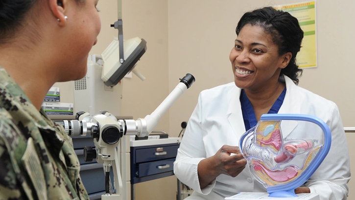 Physician holds up a model of a woman's cervix to show a patient
