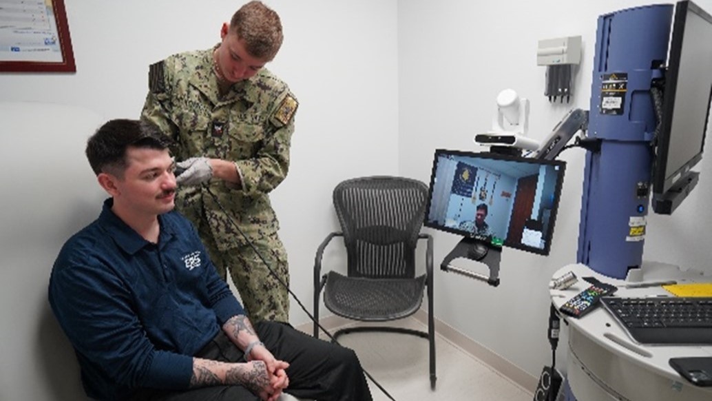 Hospital Corpsman 3rd Class Callum Wilkerson and Hospital Corpsman 3rd Class Sean File, corpsmen at the Telehealth and Medical Home Port Clinic, demonstrate a physical assessment using the Telehealth Medical Cart, which enables real-time image sharing for remote provider evaluations. (U.S. Navy Photo by Lt. Cmdr. Alicia Sacks)