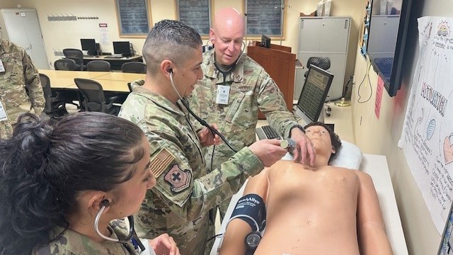 Airman 1st Class Arianna Aponte observes as Defense Health Network Central Commander Maj. Gen. Thomas Harrell and Command Chief Master Sgt. Luis Magana check a mannequin for heart and lung sounds during their visit to Keesler Medical Center, Biloxi, Miss., May 6, 2025.