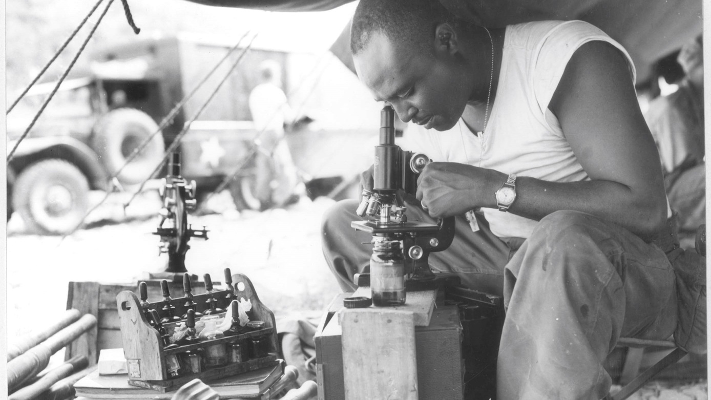 An Army laboratory technician uses a microscope to check the blood types of wounded warfighters brought in from the battlefield during the Korean war.