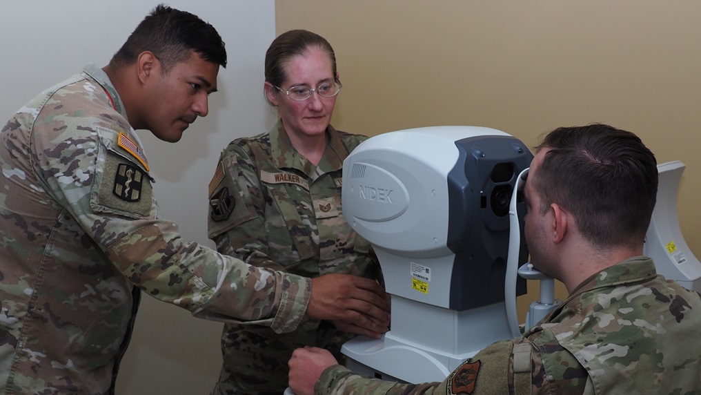 Sgt. Eduardo Morales, left, the assistant NCO in charge of the EACH Optometry Clinic, trains Air Force Tech. Sgt. Crystal Walker, and Air Force Staff Sgt. Devllin Clevenger on proper use of an auto refractor, which is used to test eye pressure and detect eye prescriptions for patients.