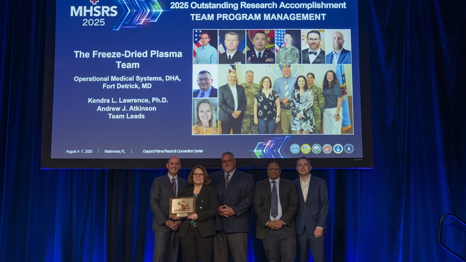 Dr. Stephen Ferrara, Acting Assistant Secretary of Defense for Health Affairs, presents the award for Outstanding Program Management (Team) to Andy Atkinson and Kendra Lawrence, Ph.D., during the Military Health System Research Symposium, Kissimmee, Florida, Aug. 4, 2025.