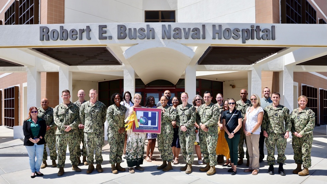 Staff and leadership from Naval Hospital Twentynine Palms gather in front of the hospital on August 20 with Commanding Officer Capt. Janiese Cleckley, Executive Officer Capt. Candace Foura, Command Master Chief HMCM Richard Moreno, Director for Public Health Cmdr. Christina Carter, and Public Health Specialist Tanya Stuckey to celebrate earning the Blue-H Award at the Gold Star level for the 14th consecutive year.