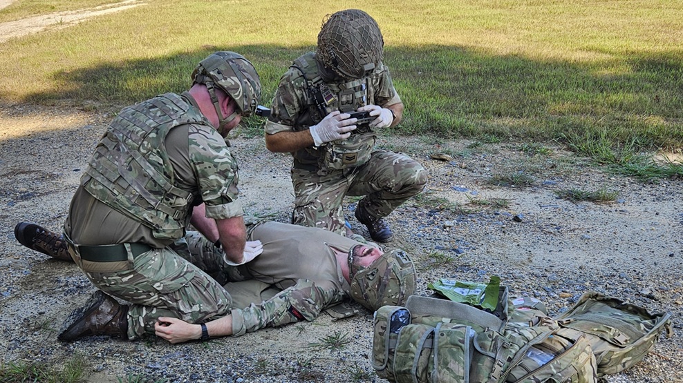 Two Soldiers kneel around one who's laying on the ground, in need of medical attention. 