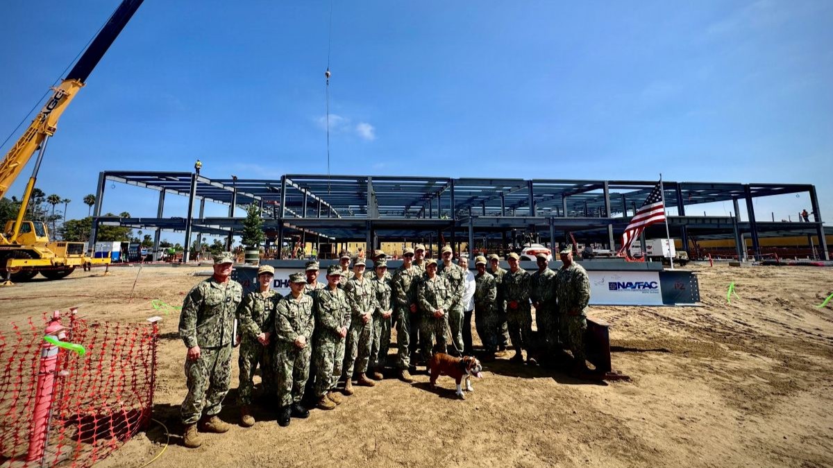 SAN DIEGO (Aug. 11, 2026) – Leadership and staff from Naval Medical Center San Diego (NMCSD) and the Marine Corps Recruit Depot (MCRD) San Diego Branch Medical and Dental Clinics gather for a group photo in front of the ceremonial steel beam during the structural steel topping out and beam-signing ceremony at MCRD San Diego, Aug. 11. Featured center is Bruno, MCRD San Diego's official mascot. The ceremony marked a major milestone in the construction of the new, state-of-the-art Branch Health Clinic, which is progressing ahead of schedule to deliver world-class healthcare facilities and support readiness for recruits, Marines, and Sailors. (U.S. Navy photo by Contributed)