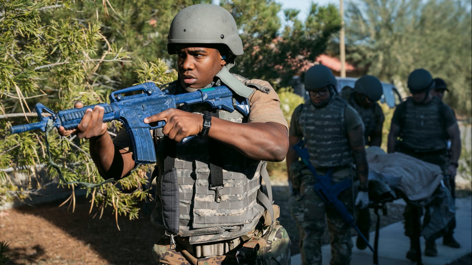 Soldier with gun; others carrying a man on a stretcher