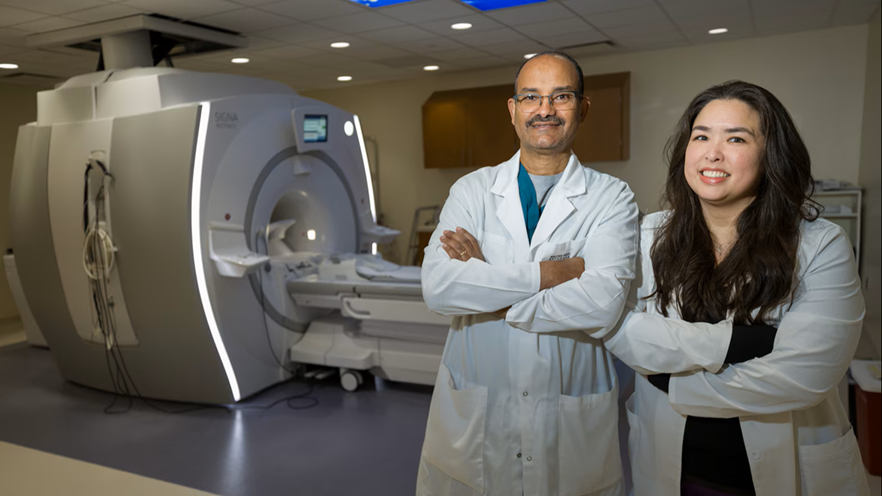 Two medical personnel stand in front of an MRI machine