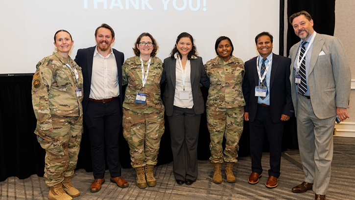 Group of people, both military and civilian, smiling in front of a sign that says "Thank You"