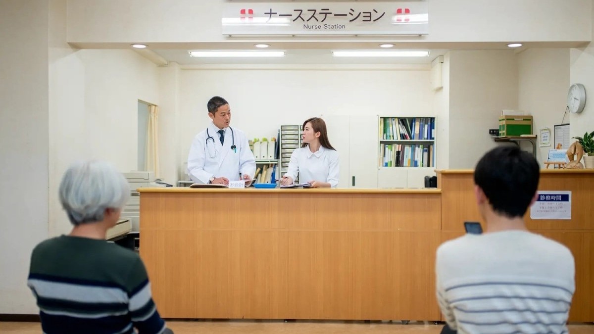 Two medical personnel at a welcome desk, with two patients in the waiting room