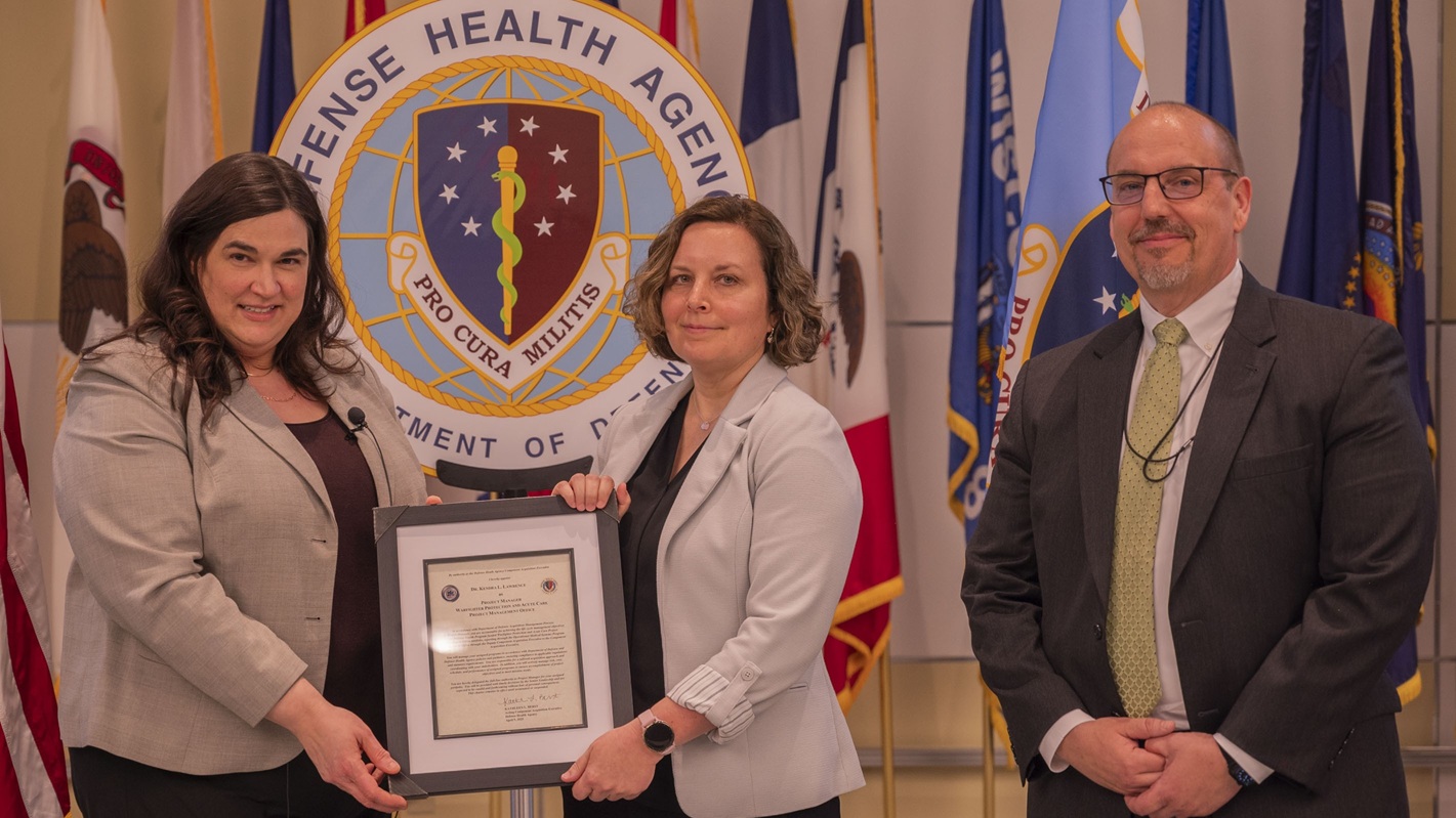Kathleen L. Berst, left, presents an official charter to Kendra Lawrence, Ph.D., during an Operational Medical Systems Program Management Office chartering ceremony, Fort Detrick, Md., April 10, 2025.