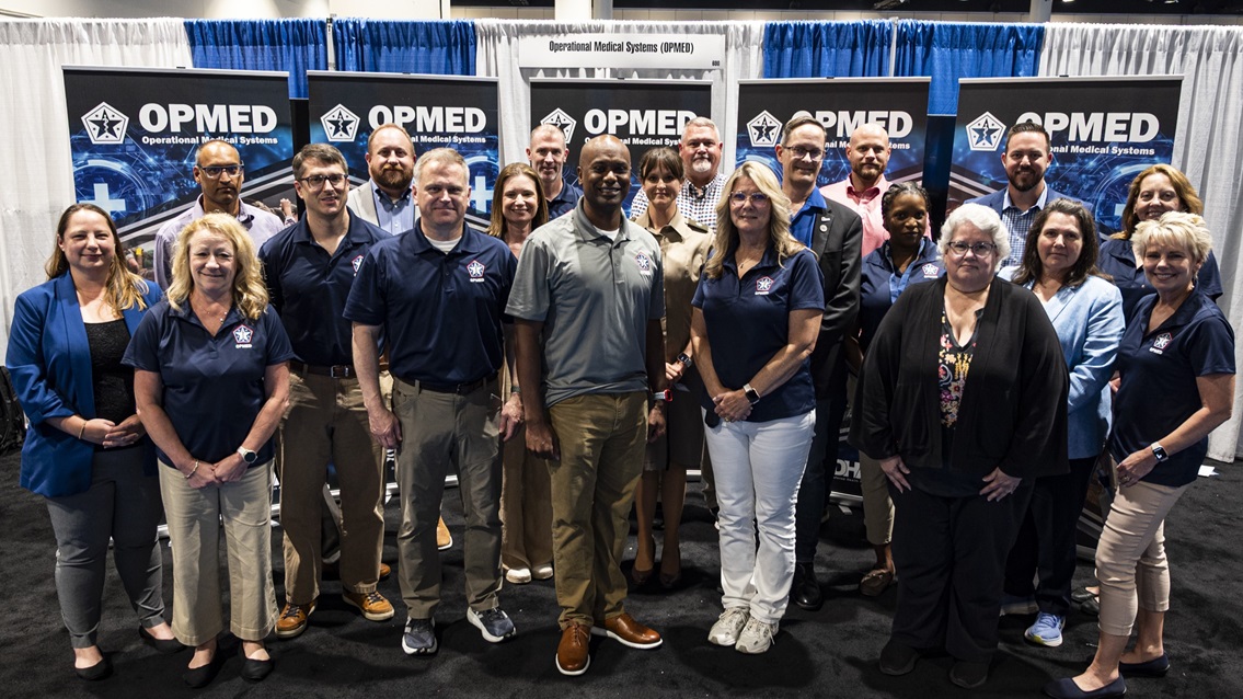 Team members with the Operational Medical Systems Program Management Office gather for a photo after the final day of exhibits during the Military Health System Research Symposium, Kissimmee, Florida, Aug. 6, 2025.